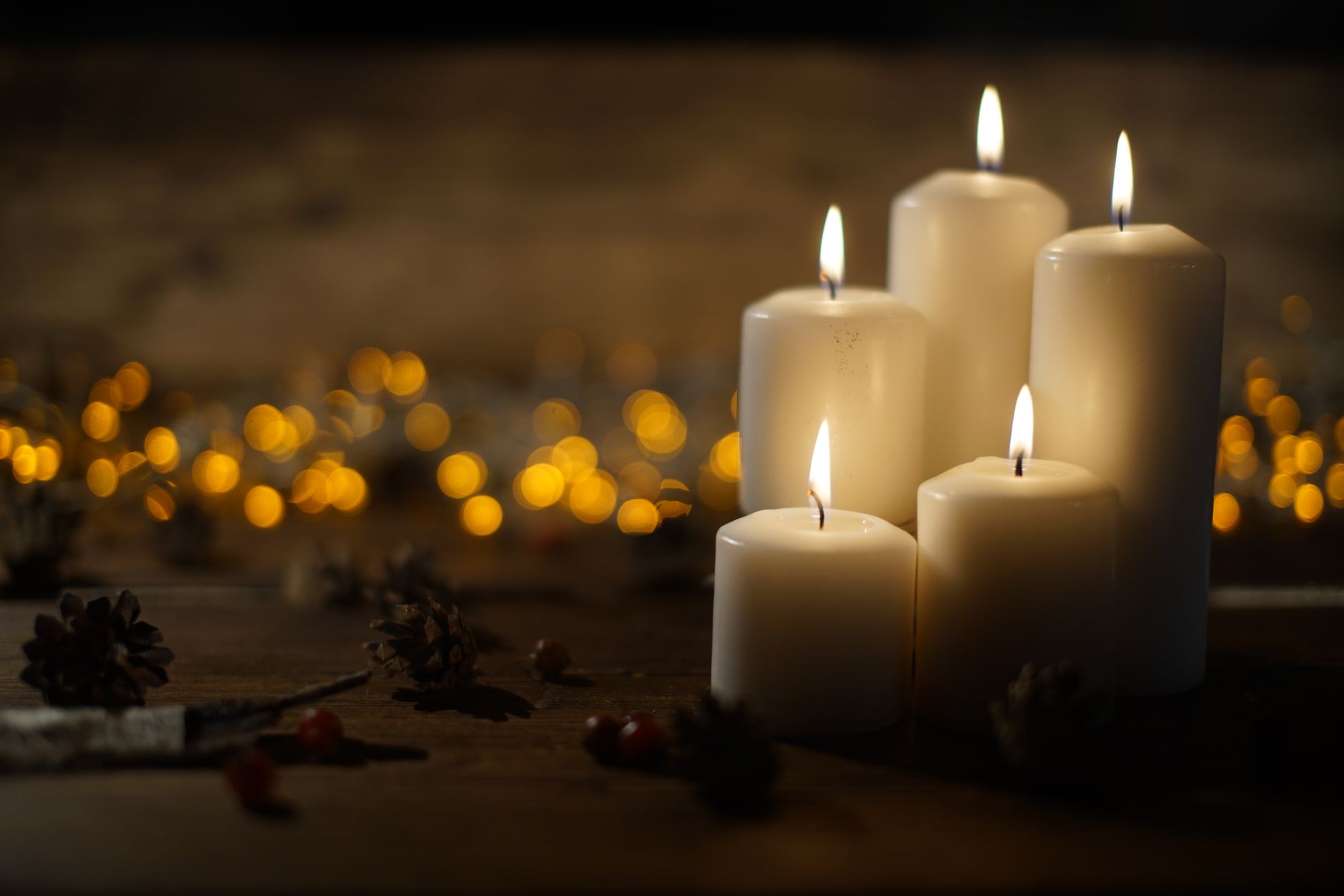 A solid beeswax pillar candle burning on a wooden table next to a wick trimmer