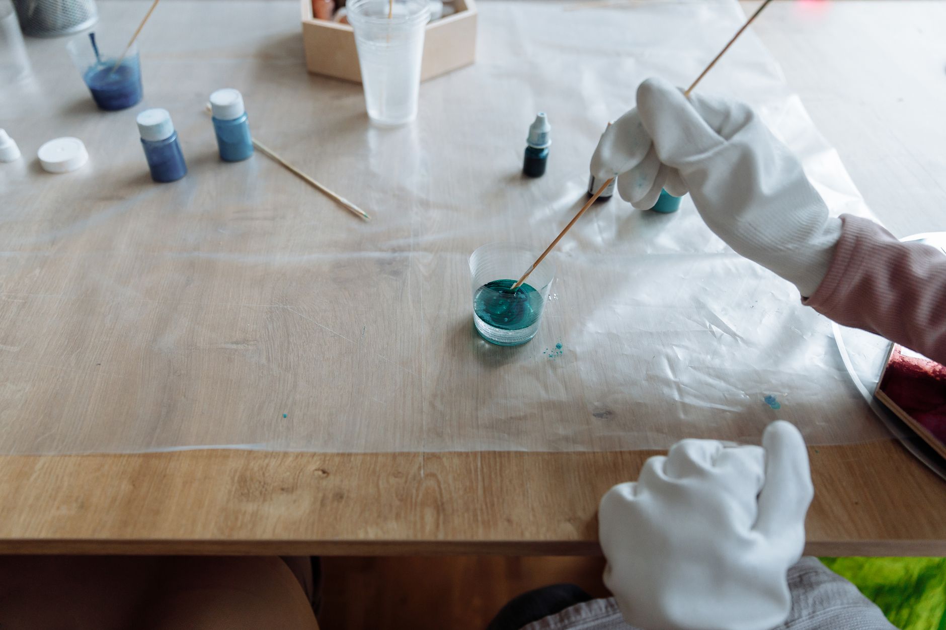 hands stirring powdered paint into water in a glass jar on a workbench